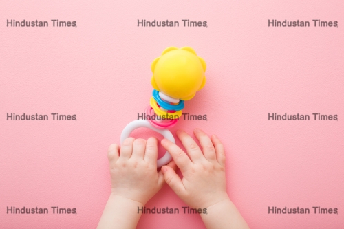 Baby,Girl,Hands,Playing,With,Colorful,Rattle,On,Light,Pink