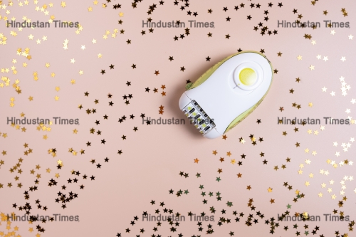 Epilator,Surrounded,By,Shiny,Foil,Confetti,On,A,Beige,Background.