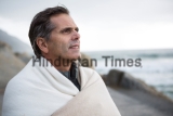 Thoughtful,Man,Wrapped,In,Shawl,On,Beach,During,Winter