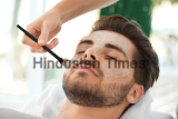 Beautician,Applying,Scrub,Onto,Young,Man's,Face,In,Spa,Salon